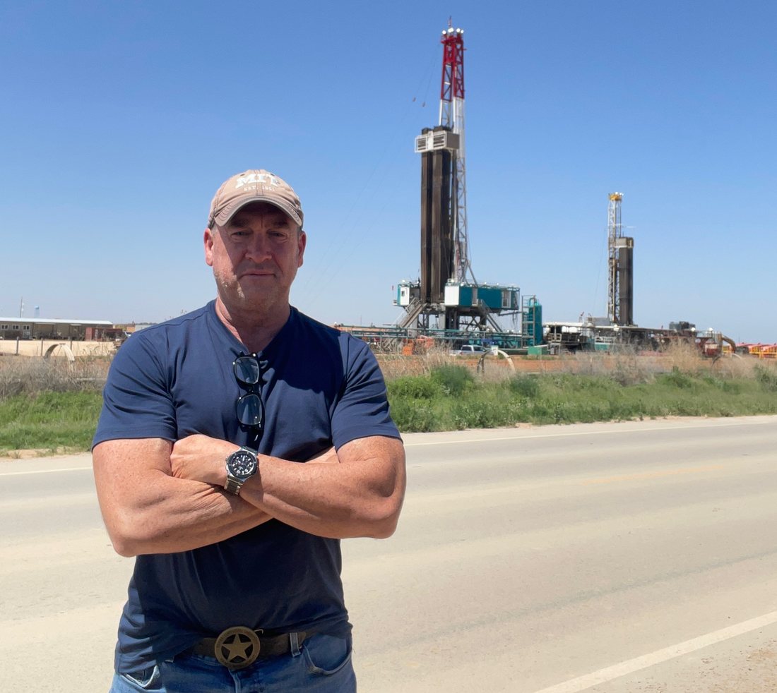 Tres Knippa, founder of HCK3 Energy, in the field at a West Texas wellsite with two drilling rigs behind him.